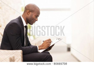 Man in suit writing on clipboard.