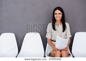 Woman sitting with paper, smiling, white chairs.